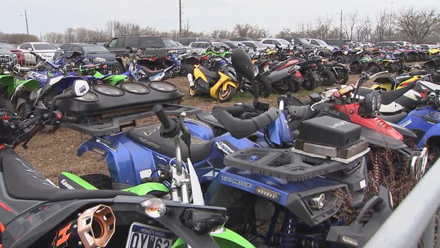 Dozens of dirt bikes and ATVs that have been confiscated, lined up in a big space 
