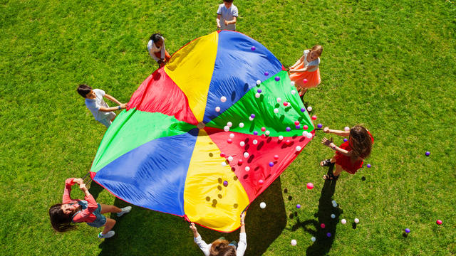 Happy kids waving rainbow parachute full of balls 
