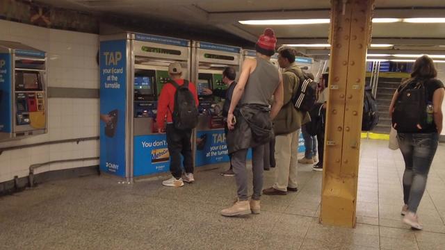 Multiple people wait in line to use MetroCard machines in the Flushing-Main Street station in Queens 