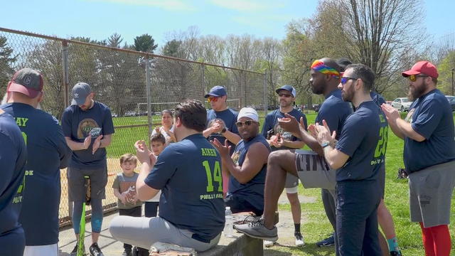Softball players sitting and standing around a bench clap 