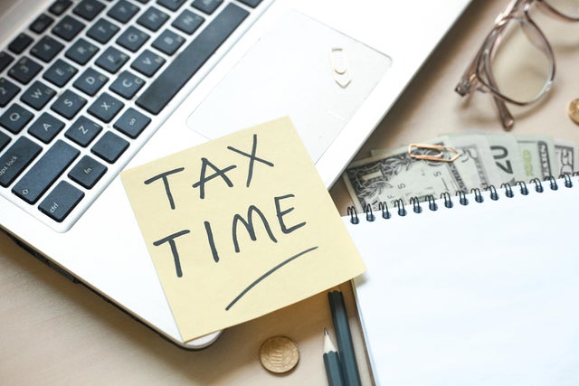Note pad with pencils, laptop, eyeglasses, money and office supplies on wooden table, concept of tax time or tax day. 