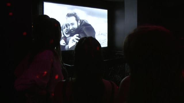 Bar patrons watch a Taylor Swift music video on a TV. 