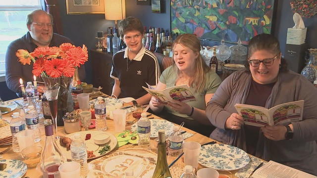A family celebrates Passover with a meal together, two people read from a prayer book at the table 