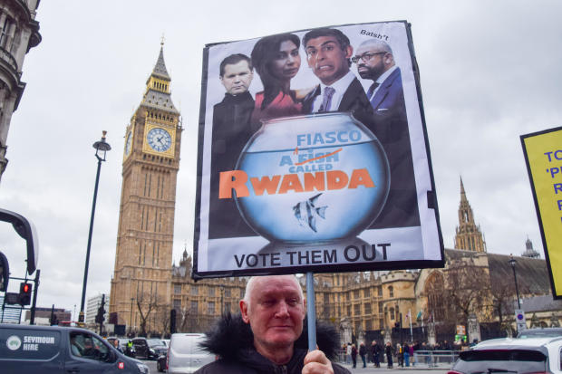 A protester holds a placard mocking the government's Rwanda 