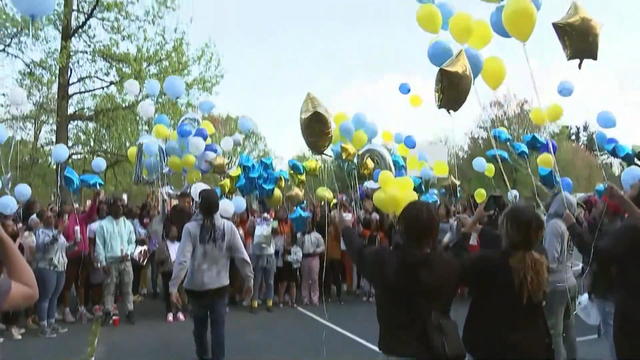 A crowd of people release yellow and blue balloons in a park 