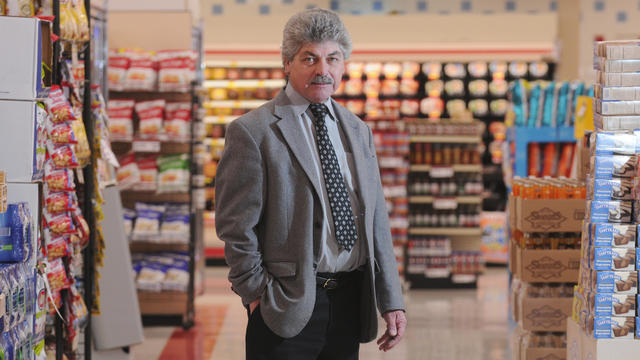 a man in a suit stands in the aisle of a grocery store 