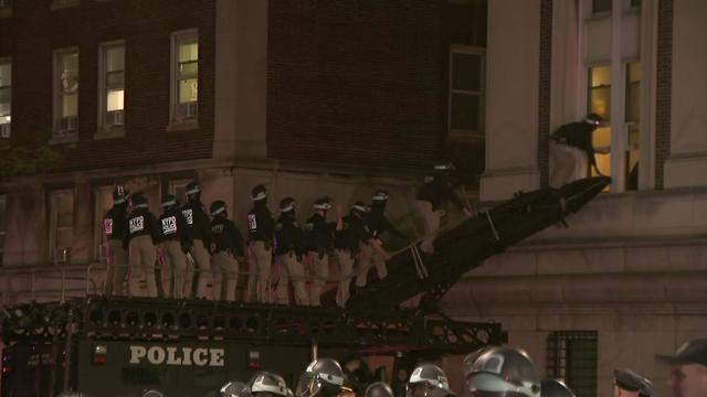 Dozens of NYPD officers walk up an Emergency Services Unit ramp to an open window of Hamilton Hall. 