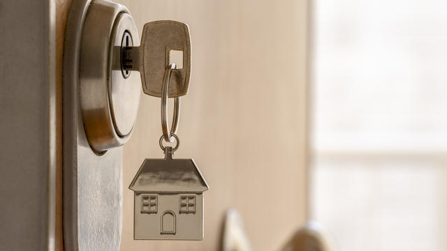 CLOSE UP OF KEY AND HOUSE KEYCHAIN ​​IN HIGH SECURITY DOOR LOCK. HOME INSURANCE CONCEPT. COPY SPACE. 