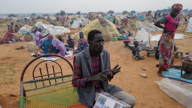 Adam Hassan, who has an album with pictures of his son and father, who he said were killed by the RSF and Arab militias in the West Darfur town of Murnei in June, sits outside his makeshift shelter in Adre 