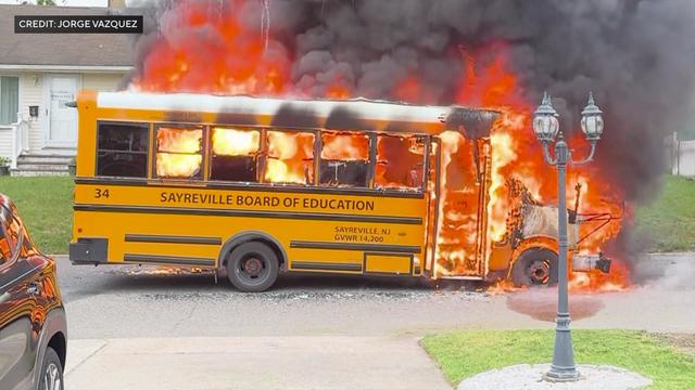 A short school bus engulfed in flames on a residential street. 