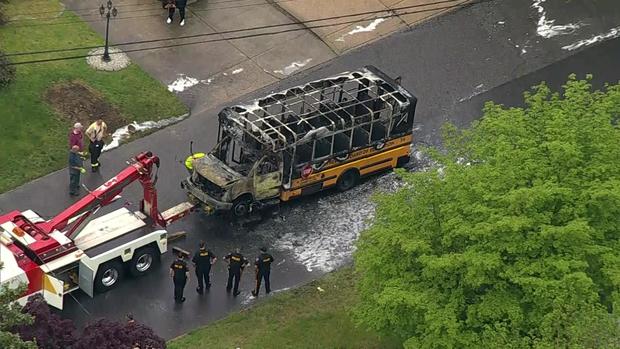 An aerial view of a school bus that has been destroyed by flames on a residential street. 