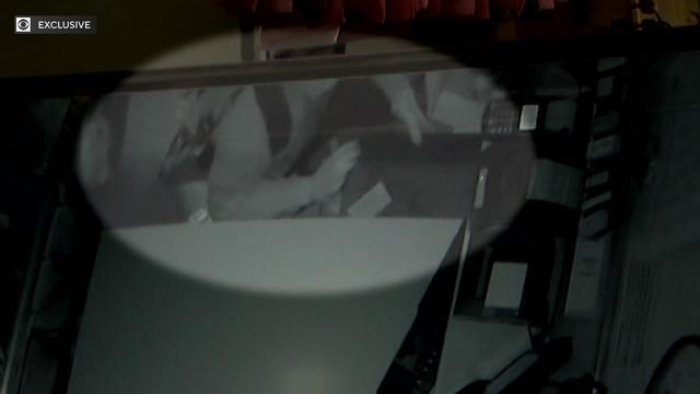 Surveillance video shows an overhead shot of an individual opening a cash register drawer. 