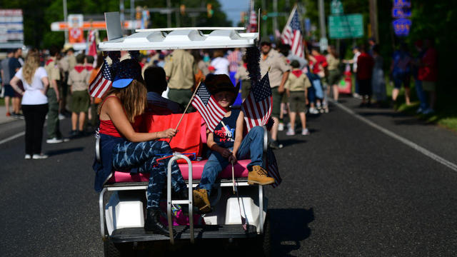 People holding small American flags ride in a golf cart during a Memorial Day parade in 2022. 