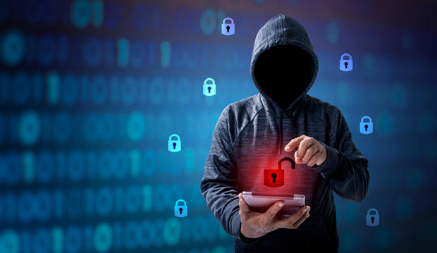 Hacker in hoodie dark theme Hacker in a blue hoody standing in front of a coding background with binary streams and information security terms cybersecurity concept 