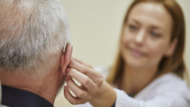 Female doctor applying hearing aid to senior man's ear 