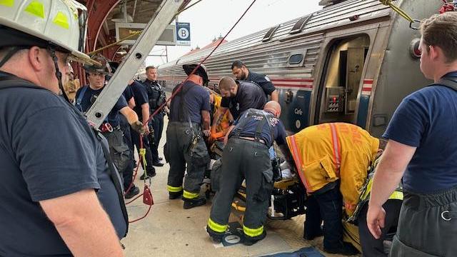 Several firefighters look on as a woman is pulled from between a train car and the station platform in Wilmington, Delaware. 