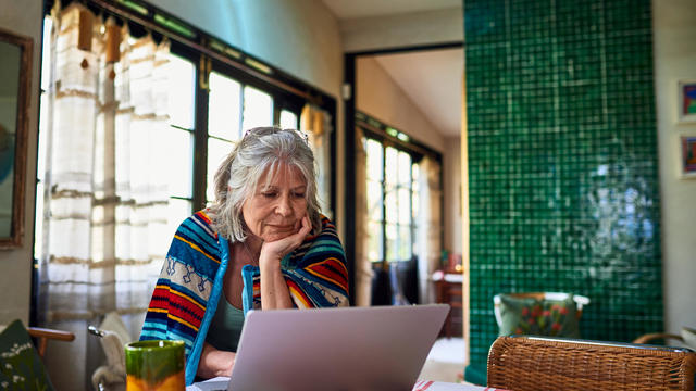 Older woman wrapped in blanket shopping online. 
