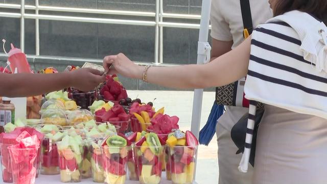 An individual hands a street vendor cash for a cup of fresh fruit. 