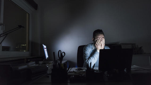 Exhausted businessman sitting at desk in office at night 