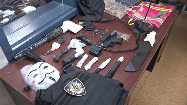 Multiple knives, an axe, NYPD body armor, handcuffs, and more displayed on a table. 