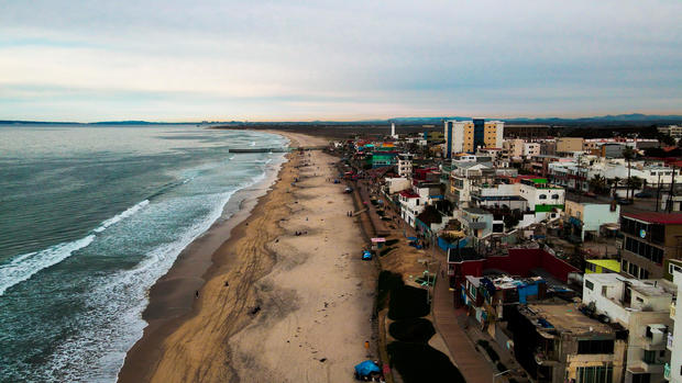 Sweeping Drone Point Of View Of The Beach And Malecon Boardwalk Near The International Border Wall In Playas Tijuana, Mexico 