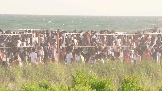 Video shows hundreds of teenagers hanging out on a beach near volleyball nets. 