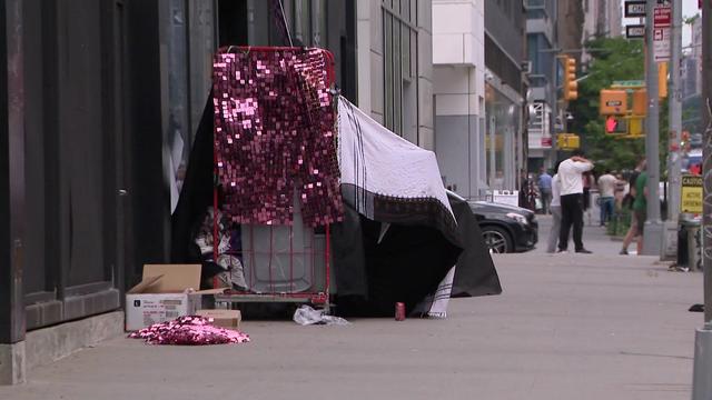 Several blankets, a cart and other miscellaneous items are used to create a tent on a New York City sidewalk. 