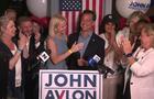 John Avlon stands behind a podium surrounded by supporters. 