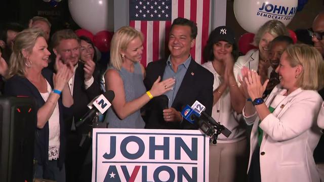 John Avlon stands behind a podium surrounded by supporters. 
