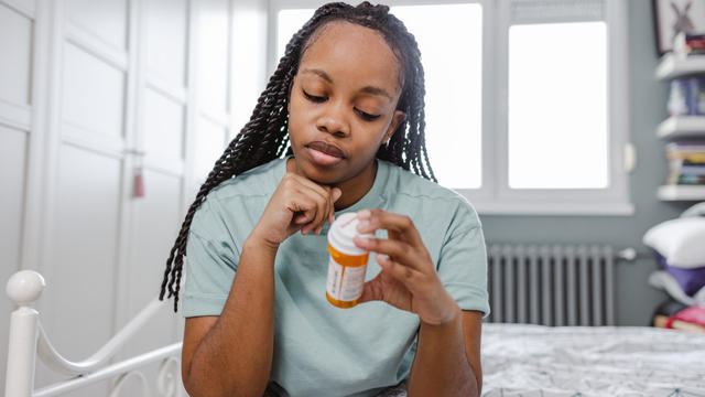 Sad African American woman holding a bottle of medicines 