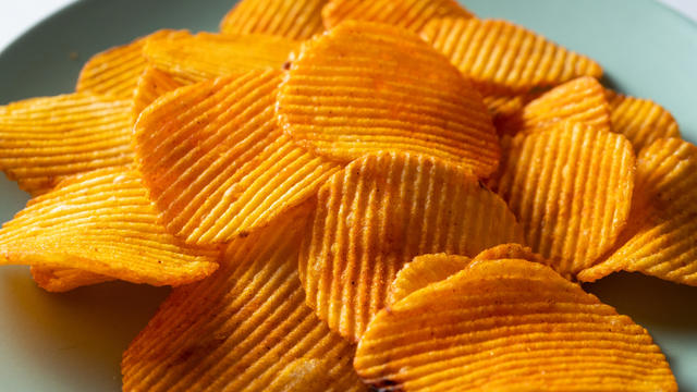 Crispy fried potato chips in a bright ceramic bowl or plate, on a white background or table. Corn spicy fatty chips with paprika and spices. The concept of unhealthy diet and lifestyle, accumulation of excess weight. Copy space. Background of food. 