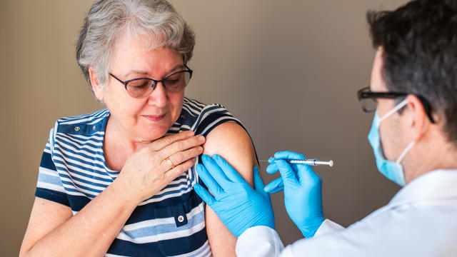 Older woman getting injected with a vaccine by doctor in upper arm. 