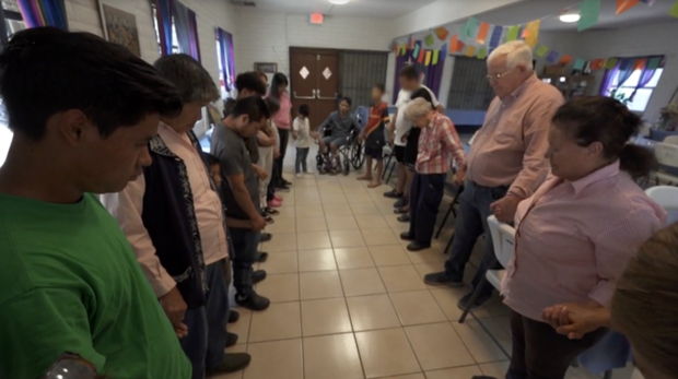 Ruben Garcia and migrants at one of the Annunciation House shelters in El Paso pray before enjoying a meal cooked by American volunteers. 