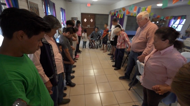 Ruben Garcia and migrants at one of the Annunciation House shelters in El Paso pray before enjoying a meal cooked by American volunteers.