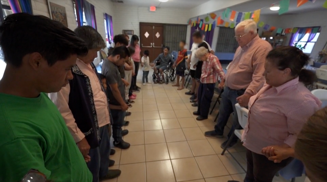 Ruben Garcia and migrants at one of the Annunciation House shelters in El Paso pray before enjoying a meal cooked by American volunteers.