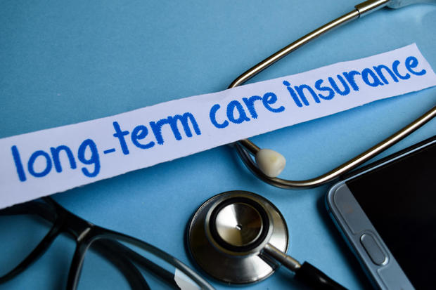 Long-term care insurance inscription with the view of stethoscope, eyeglasses and smartphone on the blue background 