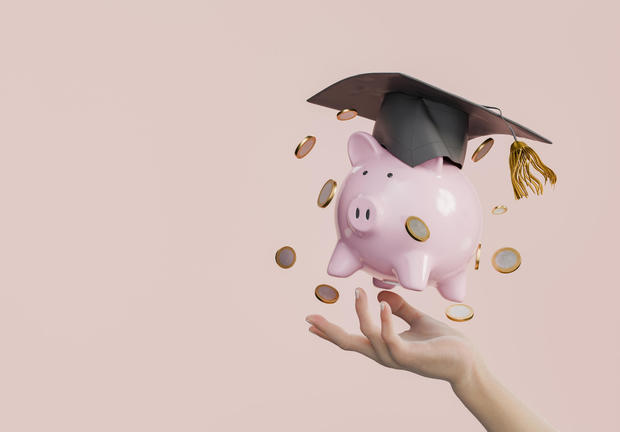 Pink Piggy Bank with Graduation Stamp and Coins in Hand on Pink Background 