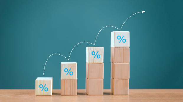 Interest rate financial and mortgage rates concept. Wood cube block increasing with icon percentage symbol upward direction on blue background. Bank business, inflation percent rate growth up arrow 