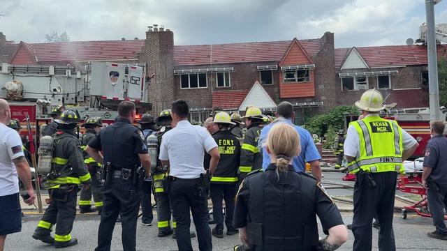 Dozens of FDNY officials stand outside a Queens Village home that has suffered fire damage. 