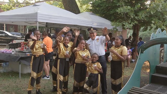 Police Commissioner Kevin Bethel poses for a photo with a group of young performers, they're all waving and smiling 