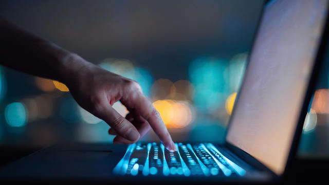 Close up of woman's hand typing on computer keyboard in the dark against colourful bokeh in background, working late on laptop at home 