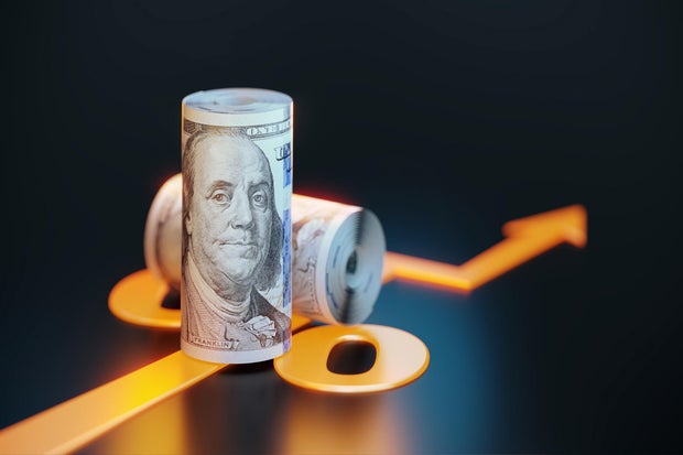 Rolled Up 100 American Dollar Bills Sitting Over Orange Colored Arrow Symbol On Black Background