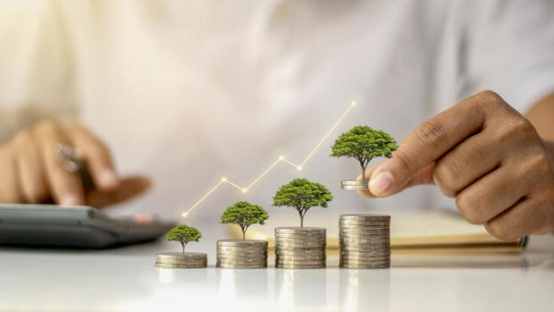 A businessman holding a coin with a tree that grows and a tree that grows on a pile of money. The idea of maximizing the profit from the business investment. 