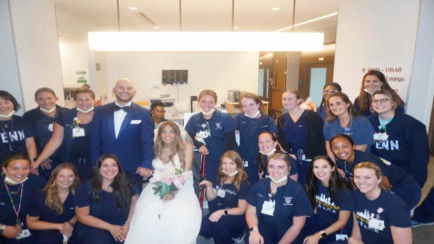 Alexis is in the middle wearing a wedding dress with her husband beside her, they're surrounded by Penn staff 