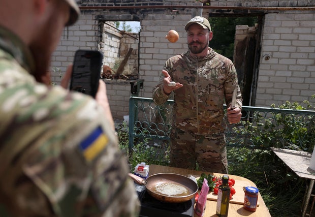 Ukrainian serviceman Ruslan Mokrytskyi cooks pasta as a fellow soldier records video of him for TikTok at an undisclosed location in Ukraine's Donetsk region