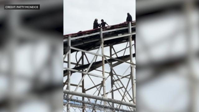 An adult leads a 12-year-old girl down a staircase along roller coaster tracks. 