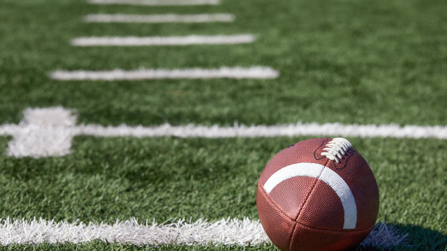 American football ball at yard line markers on playing field 