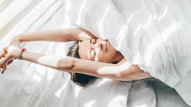 Woman sleeping under duvet at the sunny morning, top view. 