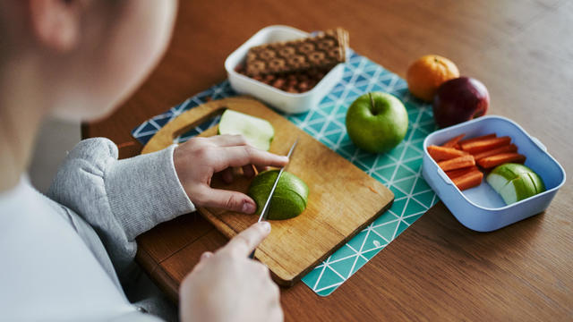 A 12-year-old schoolgirl cuts carrots and apples, prepares lunch box for school 