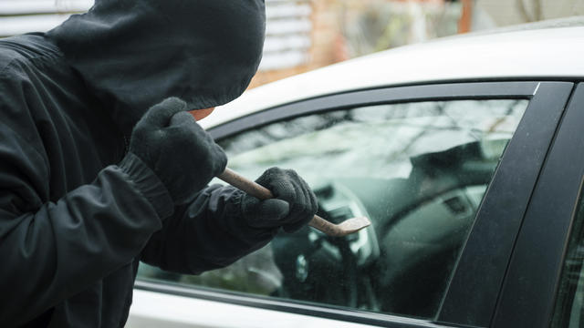 Close-up of a thief wearing balaclava breaking car window with crowbar. Car thief, car theft concept 